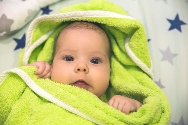 Beautiful newborn baby wrapped in a green towel after bathing