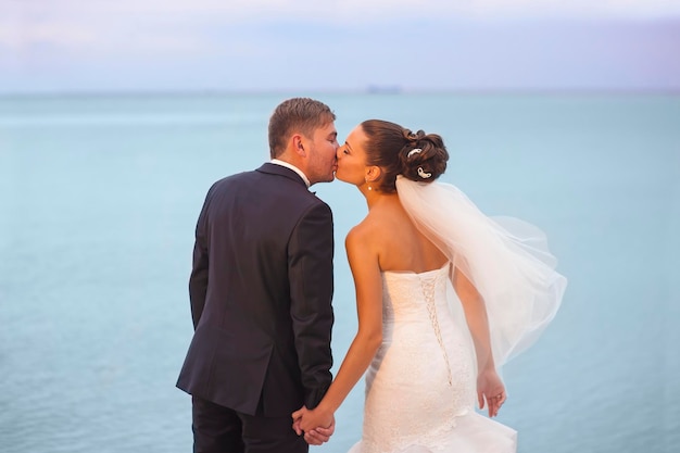 Beautiful newlyweds are holding each other by hands in sunshine and kissing