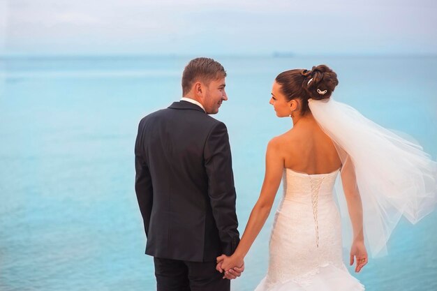 Beautiful newlyweds are holding each other by hands in sunshine