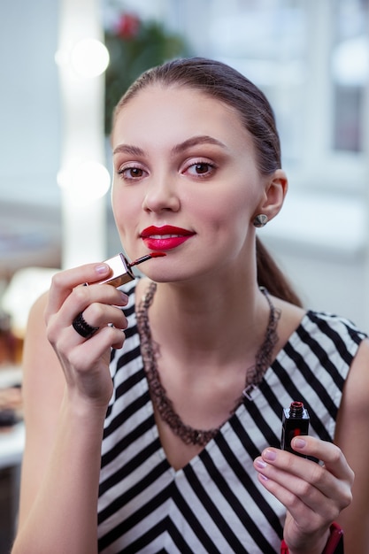 Beautiful nice woman being in a good mood while applying her lipstick