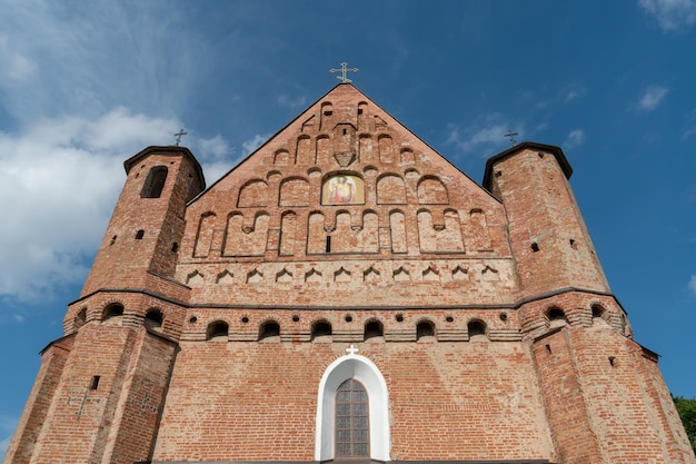 A beautiful old fortress church made of red brick against a
blue sky background a high impregnable fortress with iron crosses
on the domes arched windows and an icon in the center of the
wall