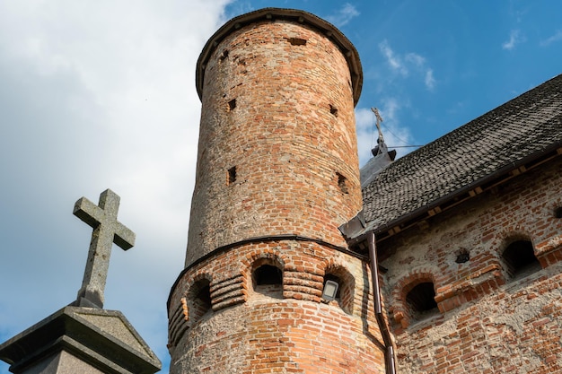 A beautiful old fortress church made of red brick against a\
blue sky background a large stone cross on the background of the\
brick wall of the old castle