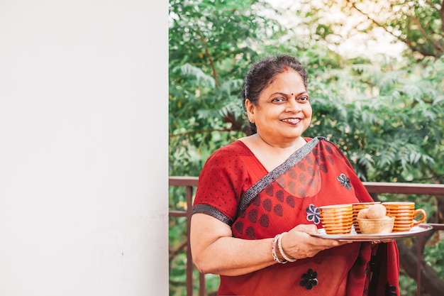 Beautiful old indian woman in a saree holding a tray with tea cups