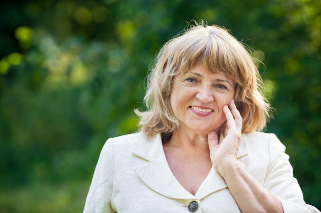 Beautiful old woman in a white suit smiles in the park