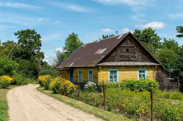 A beautiful old wooden house in the village and a cozy courtyard A wooden yellow house and flowers along a dirt road away from the hustle and bustle of the city