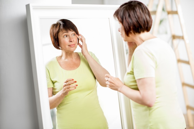 Foto bella donna anziana che si guarda il viso allo specchio