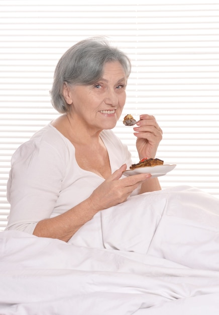 Beautiful older woman resting in the bedroom with cake