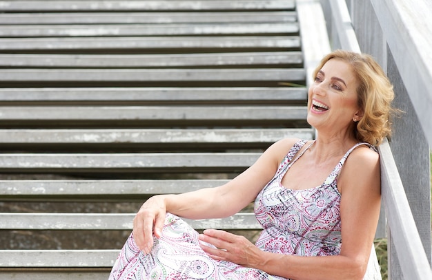 Beautiful older woman sitting on stairs and laughing outdoors