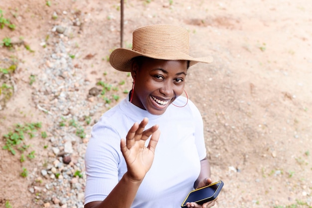 Красивая девушка онлайн-сервиса держит мобильный телефон, улыбаясь, машет рукой в камеру