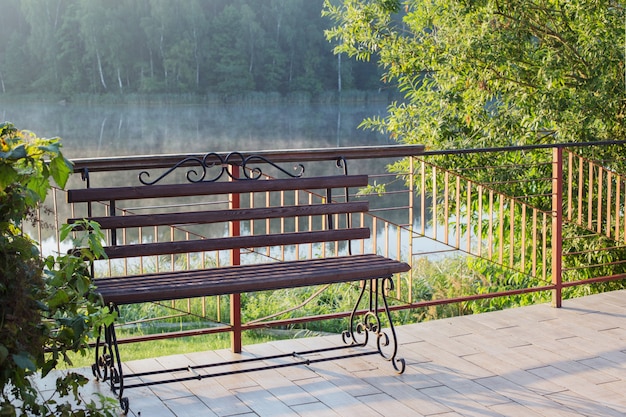 Красивая ажурная скамейка на рассвете на берегу озера летом