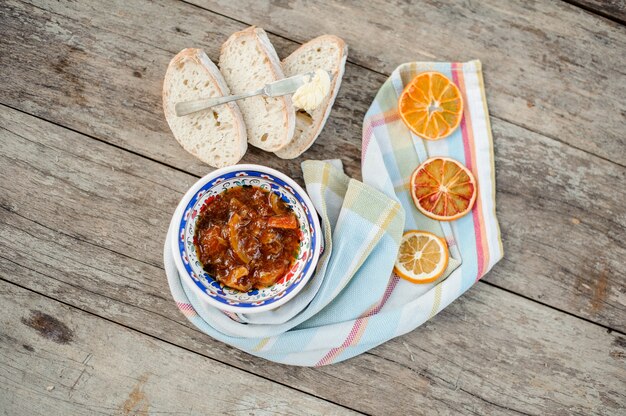 Beautiful ornate plate with a delicious orange jam on the napkin with dried oranges near the bread on the wooden table