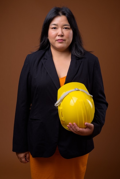 beautiful overweight Asian businesswoman holding hardhat on brown