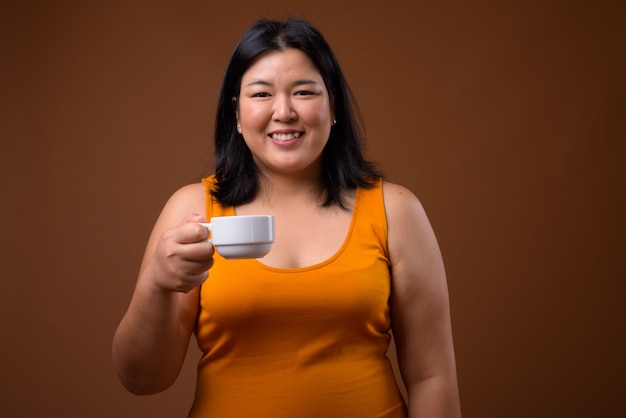 beautiful overweight Asian woman wearing orange sleeveless dress on brown