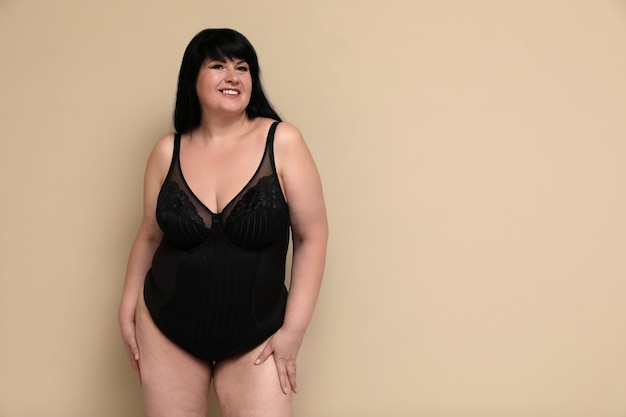 Photo beautiful overweight woman in black underwear on beige background space for text plussize model