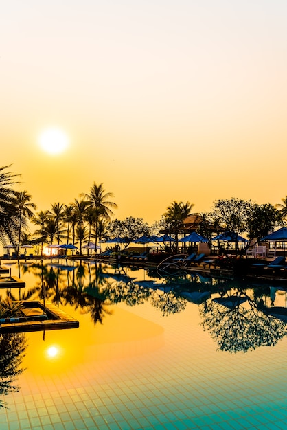 beautiful palm tree with umbrella chair pool in luxury hotel resort at sunrise times - holiday and vacation concept