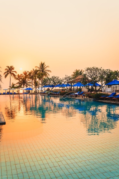 beautiful palm tree with umbrella chair pool in luxury hotel resort at sunrise times - holiday and vacation concept