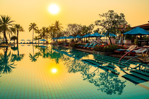 красивая пальма с бассейном с зонтиком в роскошном гостиничном комплексе во время восхода солнца - концепция отдыха и отпуска