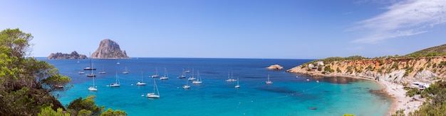 Bellissimo panorama della spiaggia cala hort e della montagna es vedra con barche a vela in mare. ibiza, isole baleari. spagna