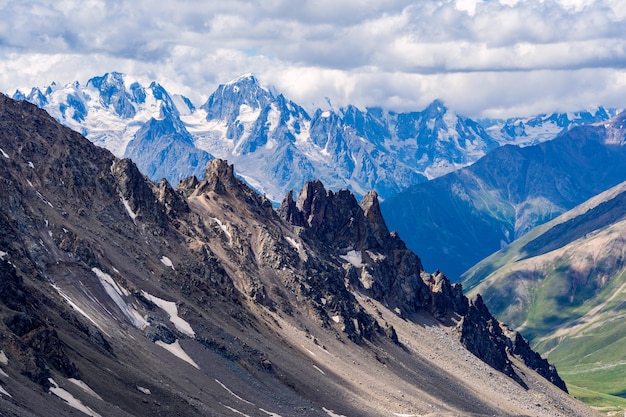 Beautiful panorama of high rocky mountains with mighty glaciers and snowy peaks against the blue sky and clouds