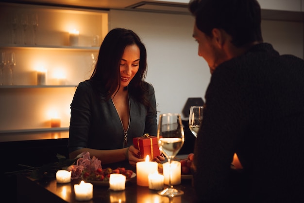 Photo beautiful passionate couple having a romantic candlelight dinner at home, drinking wine, woman getting a gift box