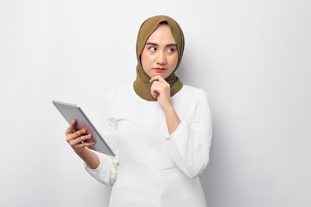 Beautiful pensive Arabian Asian Muslim woman in hijab green holding digital tablet and put hand prop up on her chin looking aside isolated on white background People religious lifestyle concept