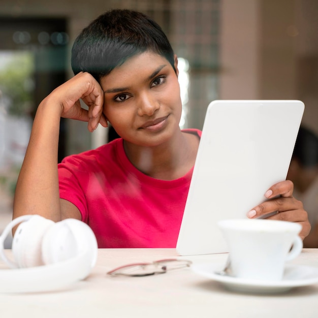 Beautiful pensive Indian woman using digital tablet communication online sitting in modern cafe