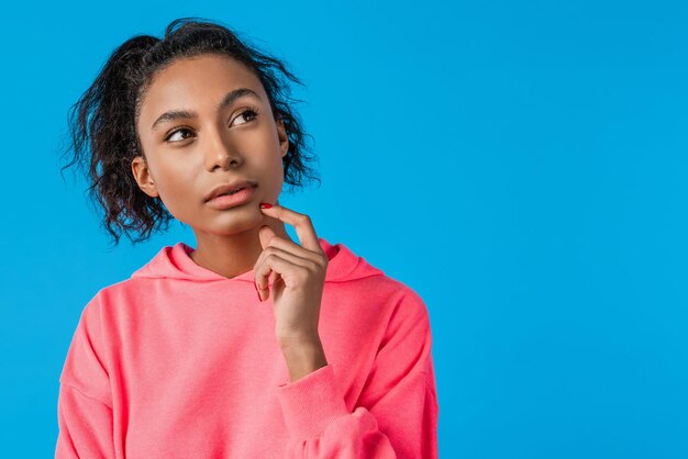 Beautiful pensive young african woman casually dressed standing isolated over blue background