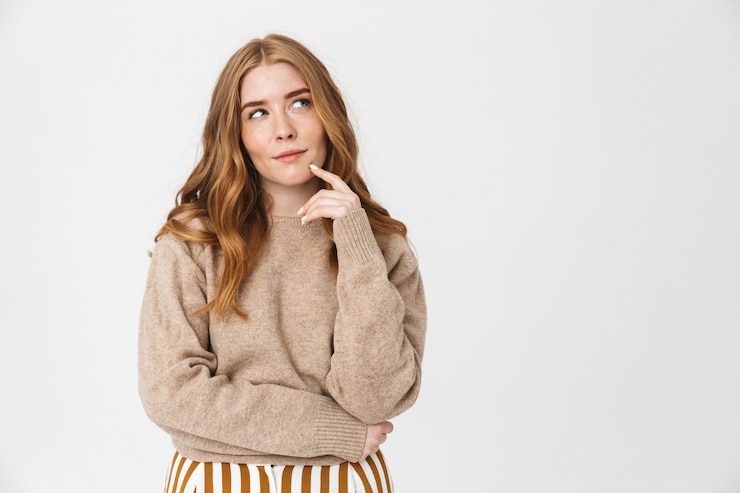 Photo beautiful pensive young girl with long blond curly hair wearing sweater standing isolated over white wall