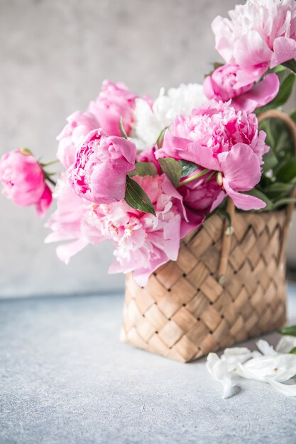 Beautiful peonies in wicker basket on wooden table