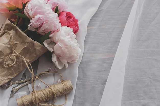 Beautiful peony bouquet twine scissors on soft fabric on dark wood top view with copy space