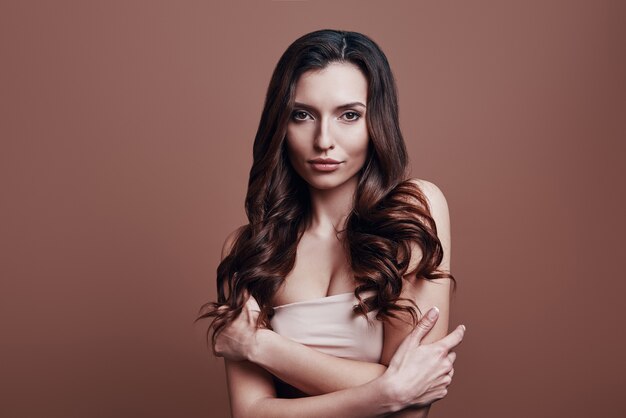 Photo beautiful perfection. attractive young woman looking at camera and smiling while standing against grey background