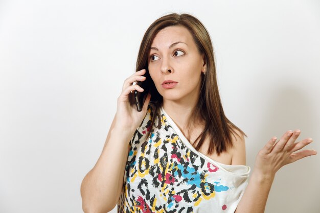 Photo the beautiful perplexed serious brown-haired woman talking on mobile phone on white background. emotions concept.