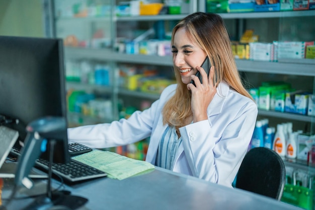 Beautiful pharmacist in uniform busy working using computer and taking calls at the pharmacy