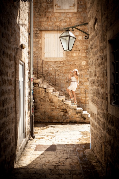 Beautiful photo on narrow street of young woman standing on stone stairs