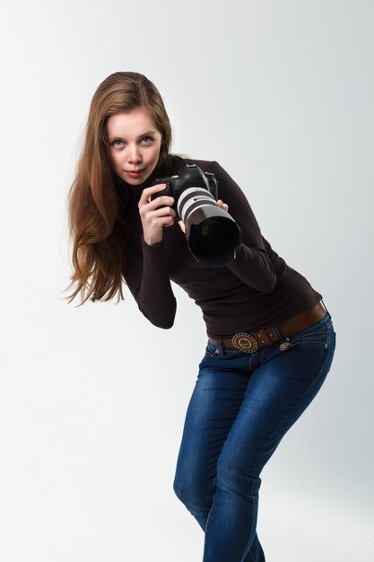 Foto la bella ragazza del fotografo con una fotocamera dslr professionale in posa su uno sfondo bianco in studio