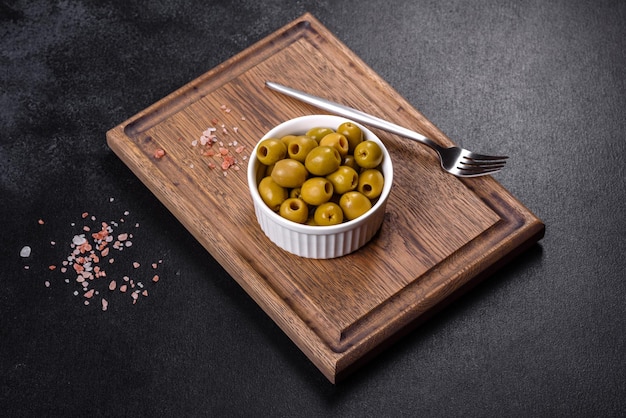 Beautiful pickled green olives on a dark concrete background. Preparation of the festive table