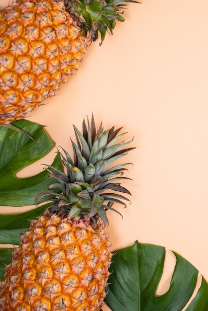 Beautiful pineapple on tropical palm monstera leaves isolated on bright pastel orange yellow background top view flat lay overhead above summer fruit