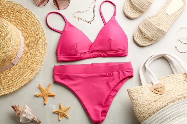 Beautiful pink bikini and beach accessories on light marble background flat lay