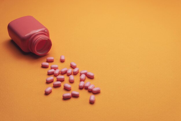 Beautiful pink bottle and pink pills on a orange background Top view