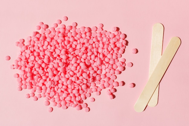 Beautiful pink depilatory wax granules and wooden spatulas on a pink background Epilation