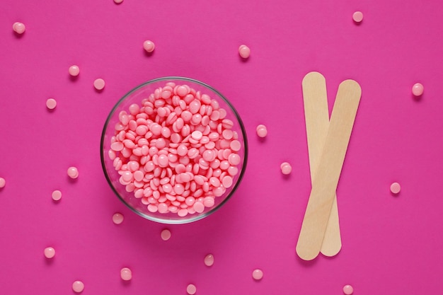 Beautiful pink depilatory wax granules and wooden spatulas on a pink background Epilation