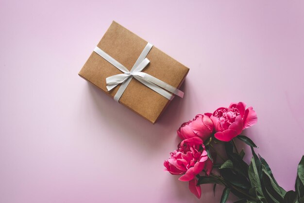 Photo beautiful pink peony flowers on a pink background and a gift box with a bow