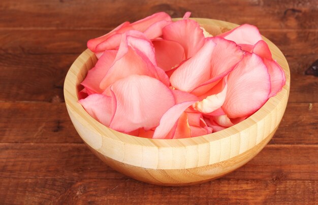 Beautiful pink rose petals in wooden bowl on table