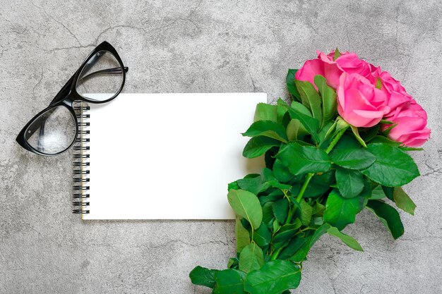 Beautiful pink roses flowers white notepad glass on concrete background