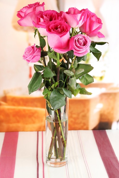 Beautiful pink roses in vase on table on room background