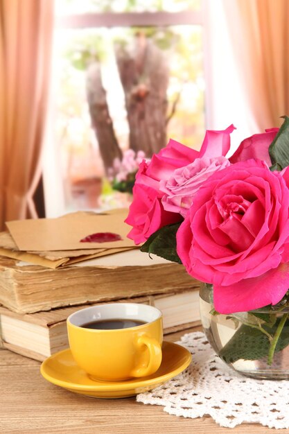 Beautiful pink roses in vase on wooden table on window background