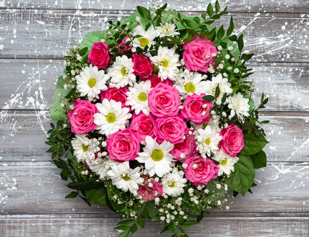 Beautiful pink roses and white daisies in a box on a gray wooden background.