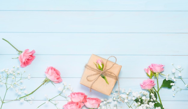 Красивые розовые розы и завернутый подарок на синем деревянном фоне