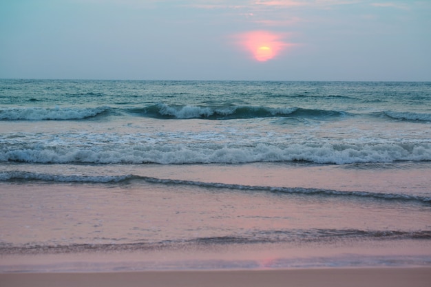 荒れ狂う海のそばの美しいピンクの夕日