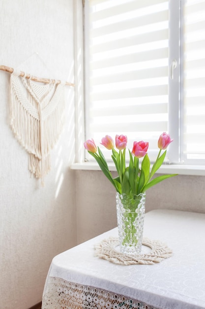 Bellissimi tulipani rosa in vaso di vetro contro wallhanging macramè fatto a mano concetto moderno ecologico all'interno